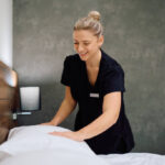 Happy chambermaid making bed in hotel room. Copy space.